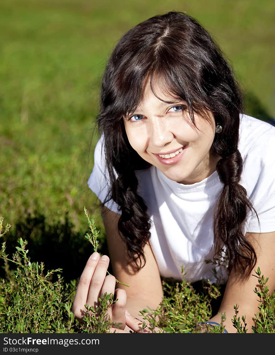 Portrait of beautiful brunette girl with blue eyes on green grass in the park.