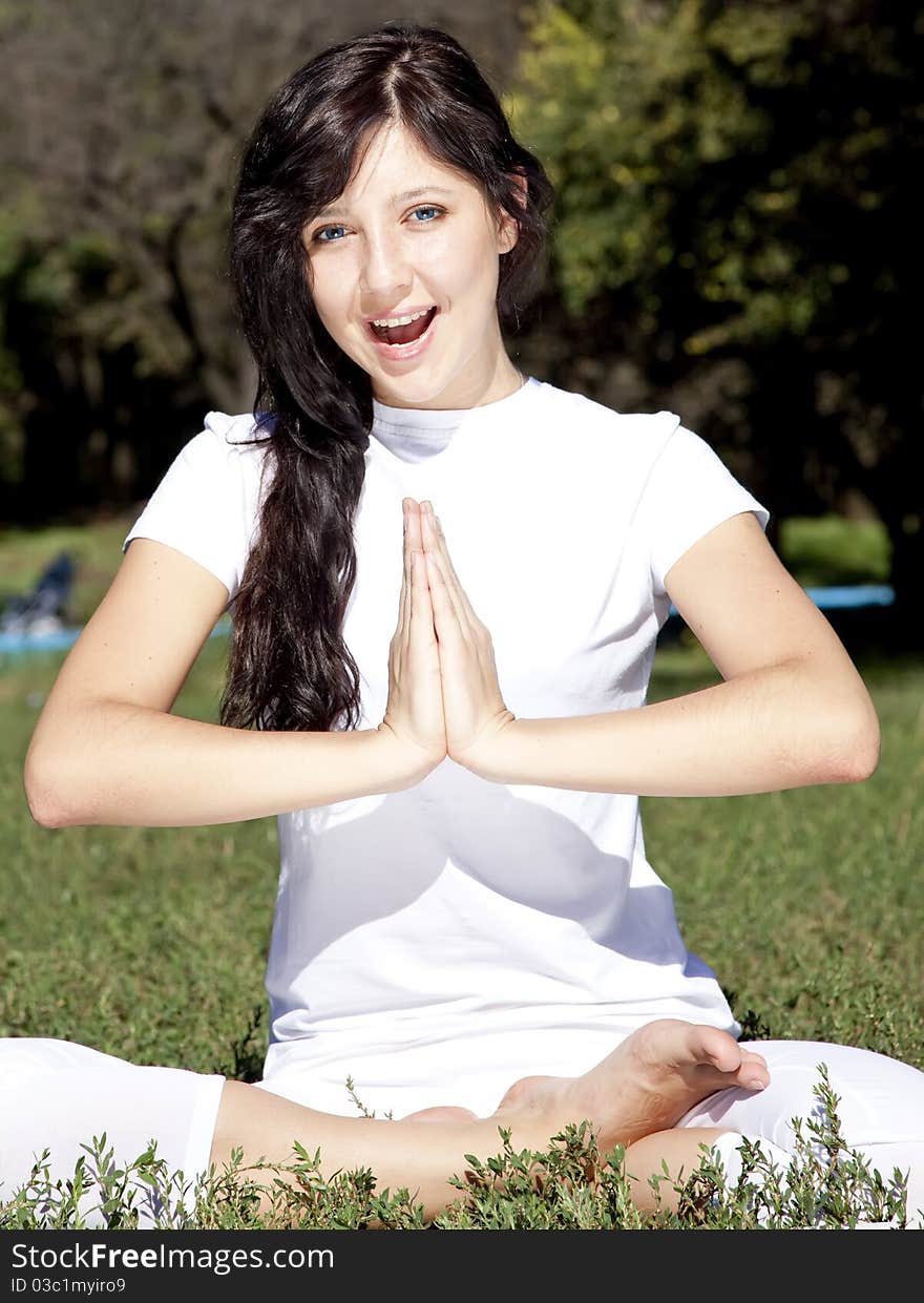 Portrait of beautiful brunette girl with blue eyes on green grass in the park.