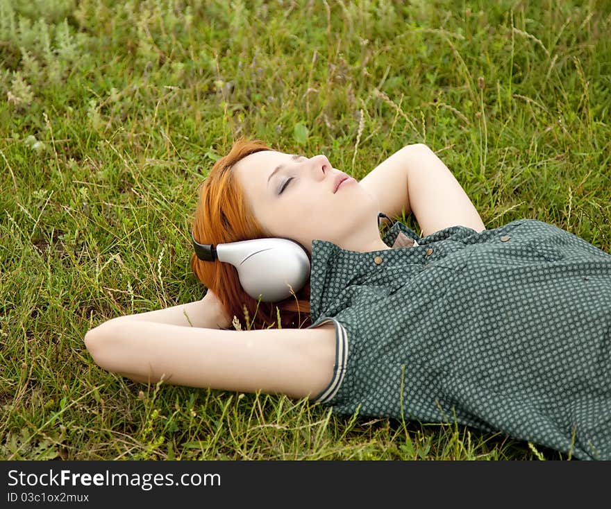 Young fashion girl with headphones lying at green grass in spring time.