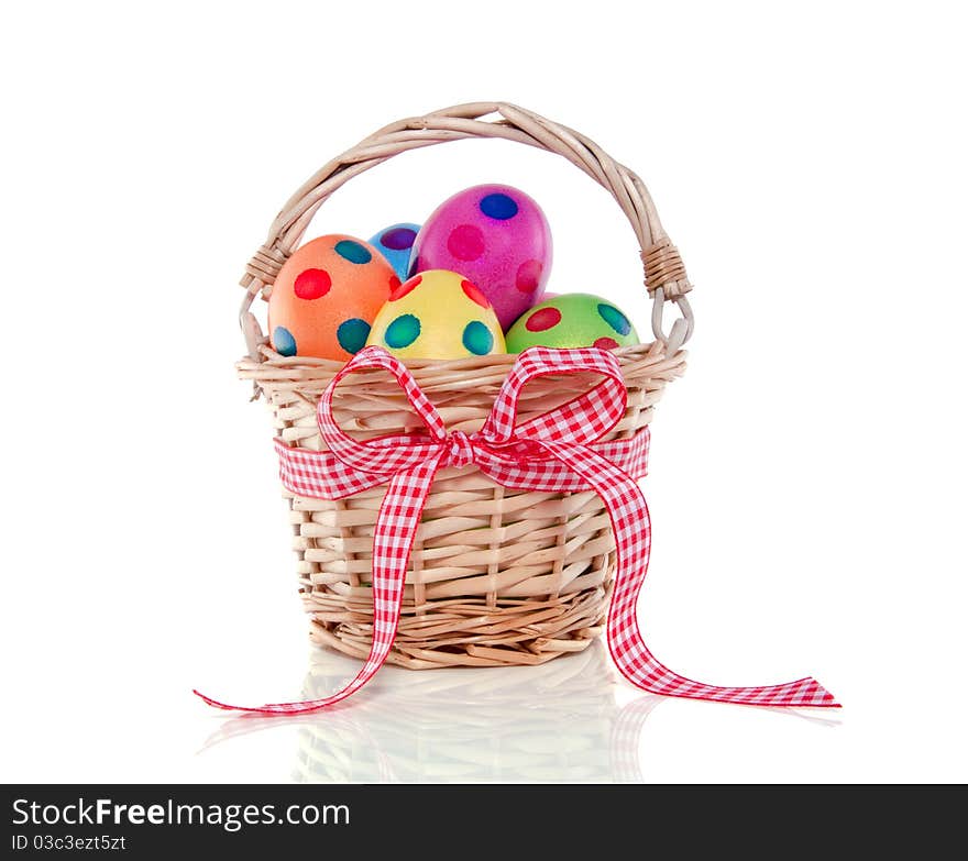 Colorful easter eggs painted with dots in a wicker basket with ribbon isolated over white