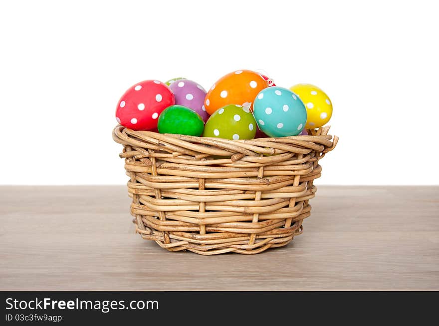 Colorful easter eggs painted with dots in a wicker basket on a table isolated over white