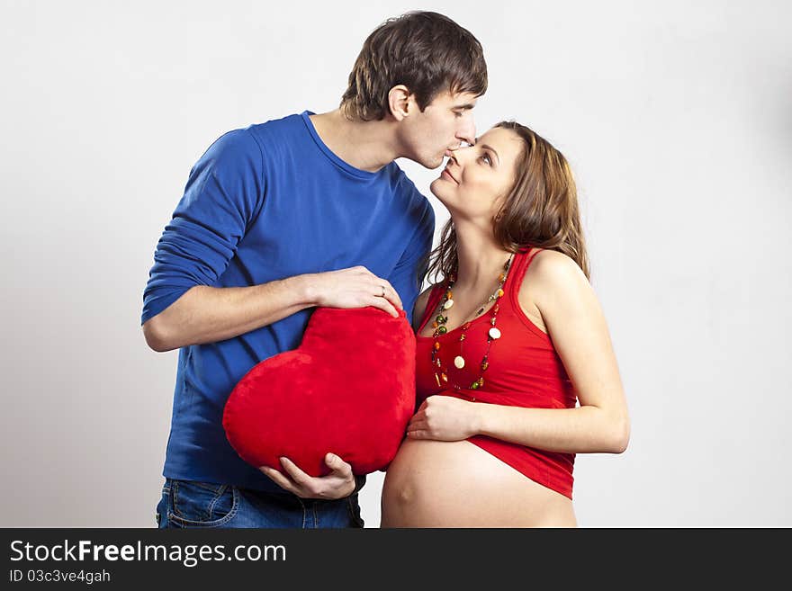 Man kissing his pregnant wife's nose holding red heart at hands. Man kissing his pregnant wife's nose holding red heart at hands