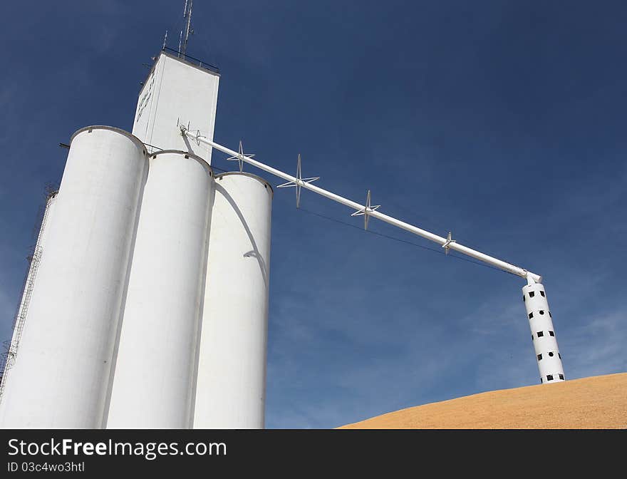 White grain elevator towering above pile of surplus corn against blue sky in the heartland.