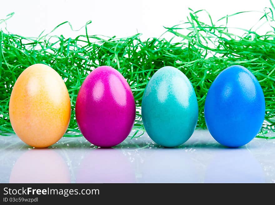 Four colored Easter eggs are on a white background with Easter grass. Four colored Easter eggs are on a white background with Easter grass