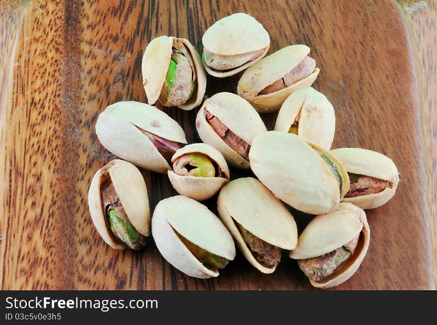 Pistachios roasted with salt lie in a wooden platter against a green background. Pistachios roasted with salt lie in a wooden platter against a green background