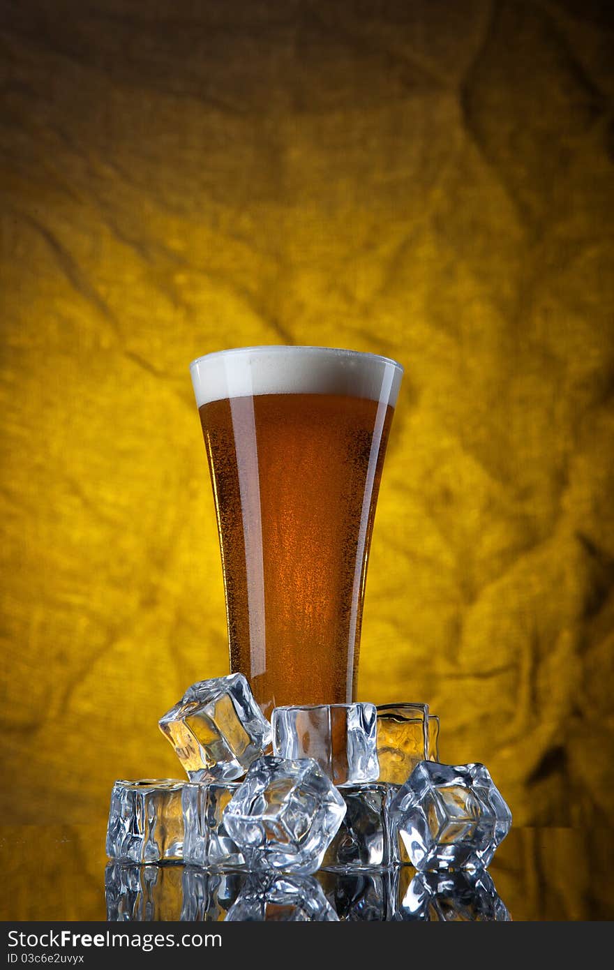 Beer in glass with ice cubes on yellow background