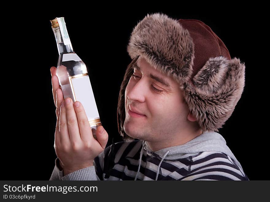 Man in a striped sweater and a fur hat with adoring looks at the bottle of alkohol