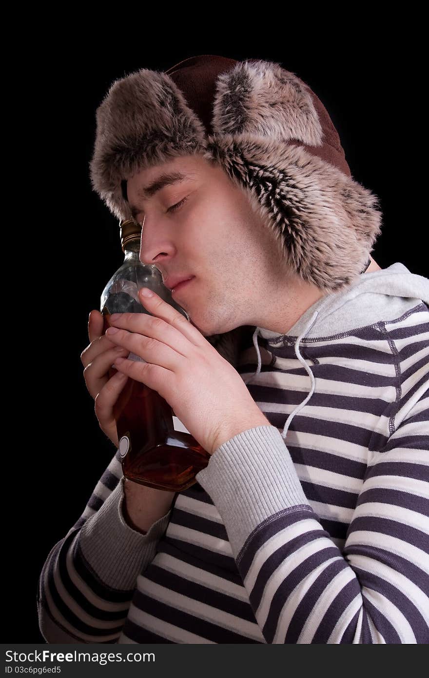 Man in a striped sweater and a fur hat with adoring looks at the bottle of alkohol