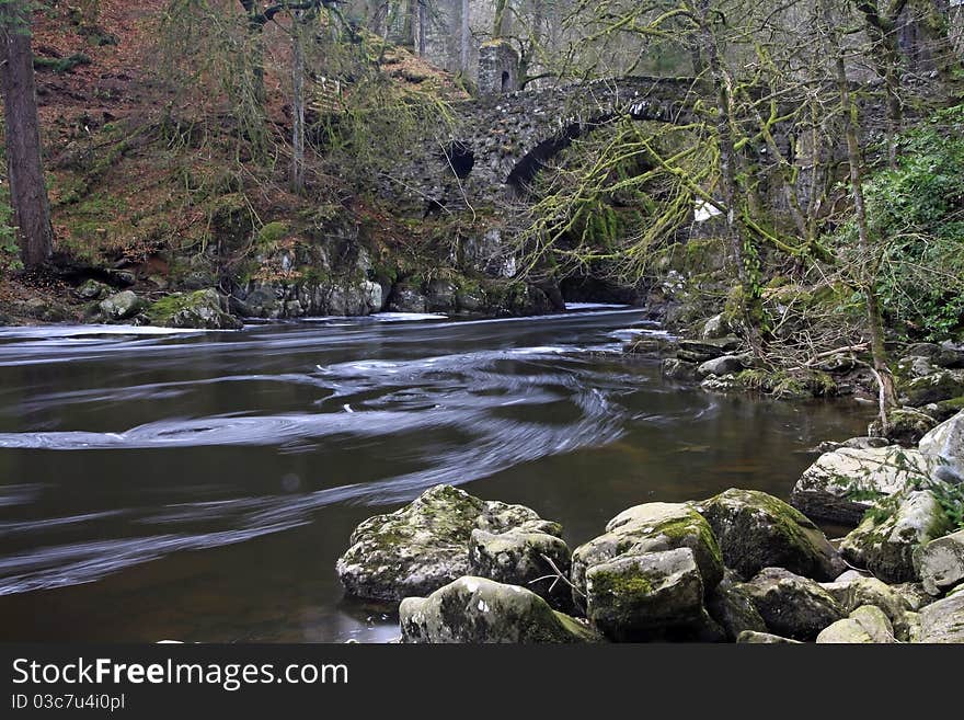 Stone bridge over waterfall in the highlands of scotland in winter with flowing water in foreground