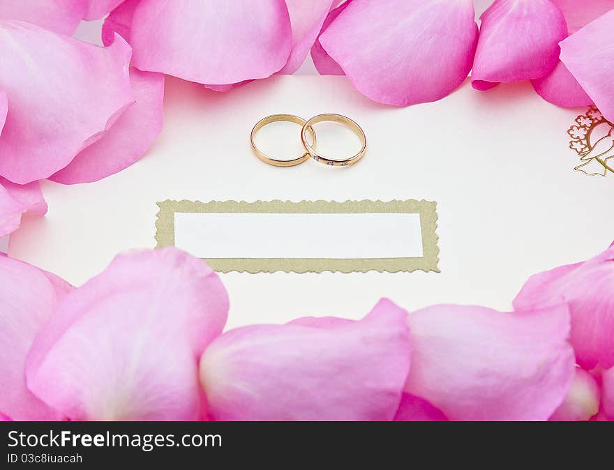 Wedding invitation in envelope with two rings, surrounded by rose leafs