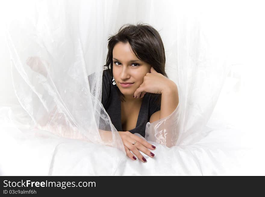 Close-up portrait of a young beautiful smiling girl with dark hair, bright nails and shining eyes, lying on the bed