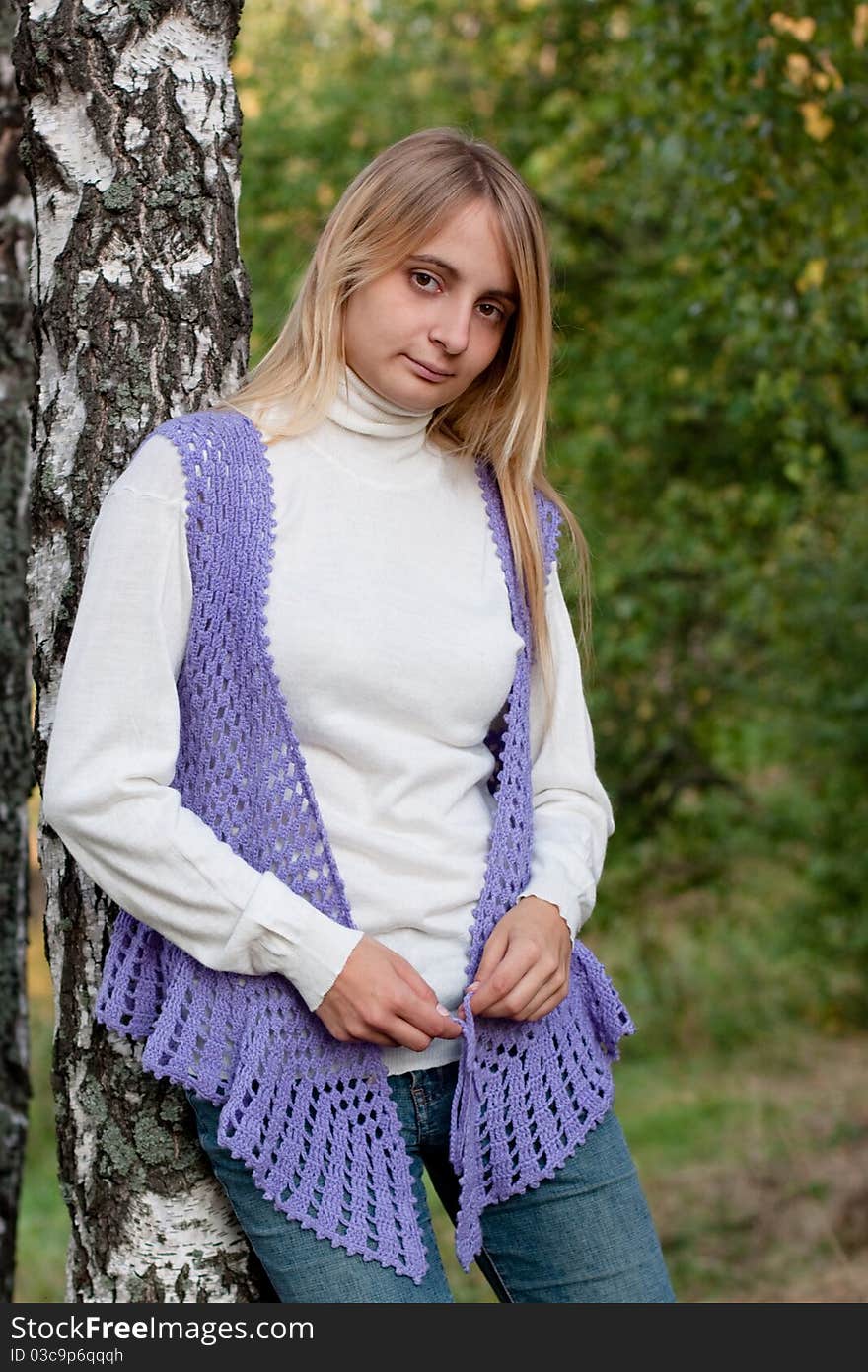 A girl in a lilac vest and white polo-neck sweater and jeans in a forest. A girl in a lilac vest and white polo-neck sweater and jeans in a forest