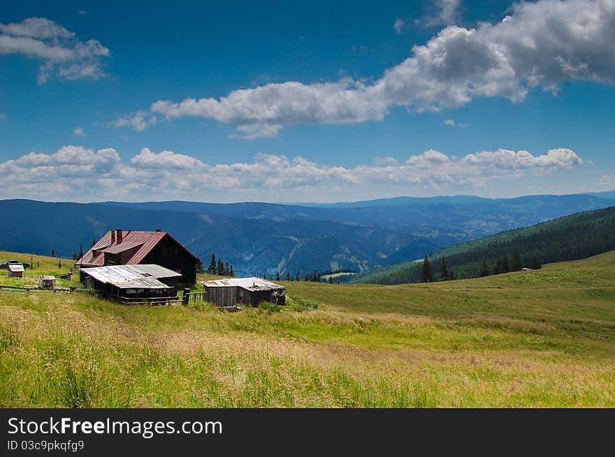 A building surrounded with green grass and high mountain peaks. A building surrounded with green grass and high mountain peaks