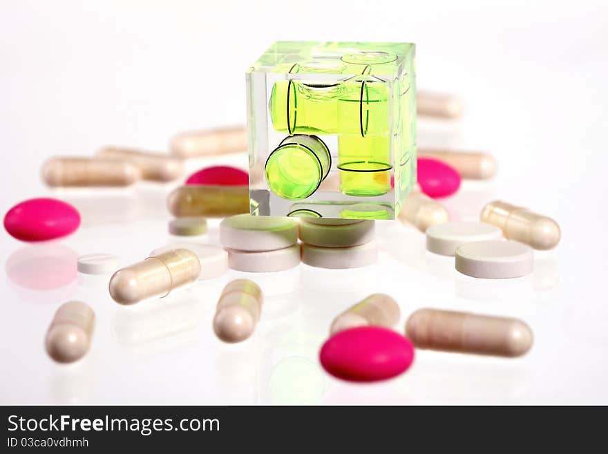 Pink and white pills on a white background with a small level on top of them. Pink and white pills on a white background with a small level on top of them