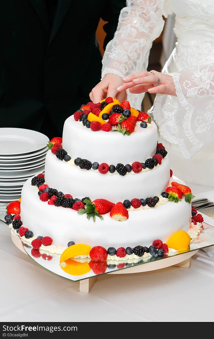 Cutting fresh wedding fruitcake with strawberries, raspberries, blackberries, peaches and blueberries