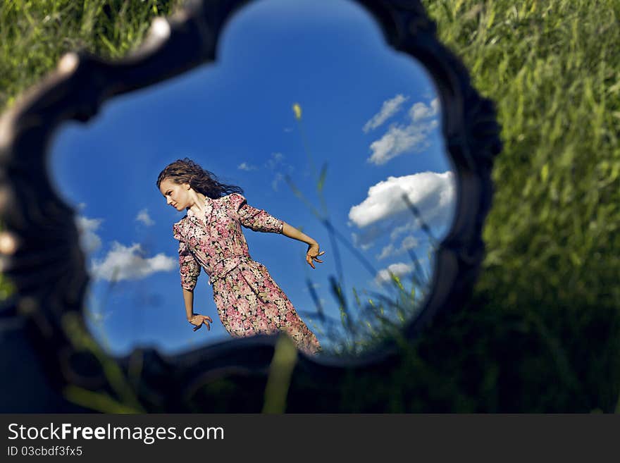 A girl stands on a background sky reflected in a mirror