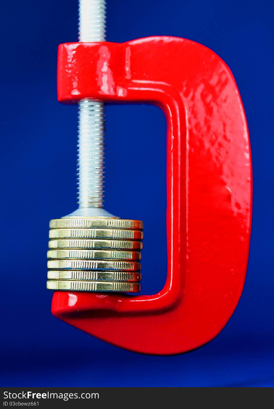 A stack of gold coins in a red clamp with a dark blue background, indicating the pressure is on to make ends meet. A stack of gold coins in a red clamp with a dark blue background, indicating the pressure is on to make ends meet.