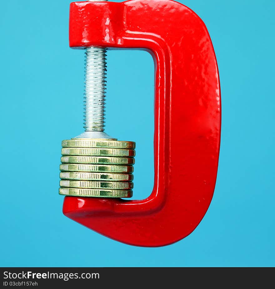 A stack of gold coins in a red clamp with a light pastel blue background, indicating the pressure is on to make ends meet. A stack of gold coins in a red clamp with a light pastel blue background, indicating the pressure is on to make ends meet.