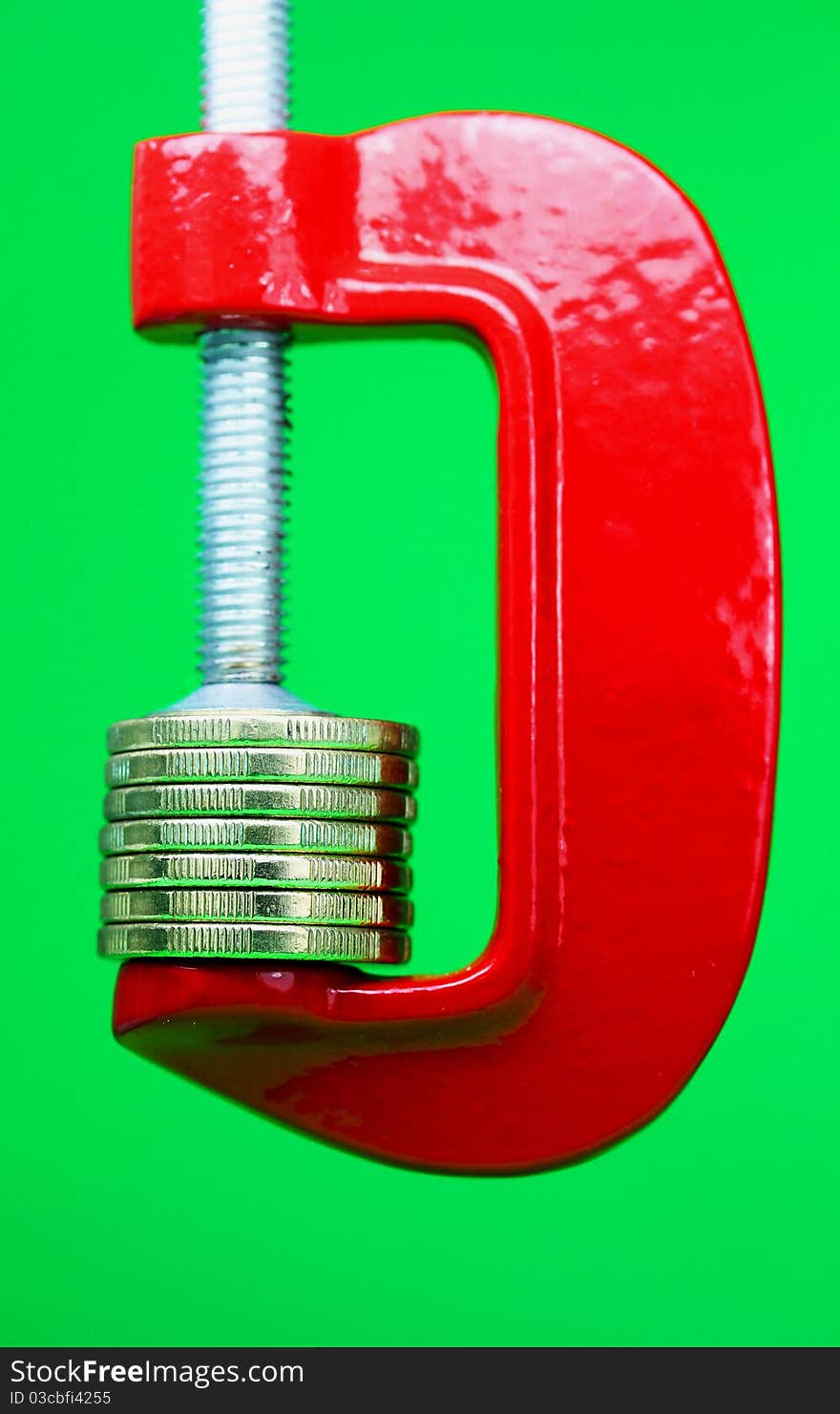 A stack of gold coins in a red clamp with a light pastel green background, indicating the pressure is on to make ends meet. A stack of gold coins in a red clamp with a light pastel green background, indicating the pressure is on to make ends meet.