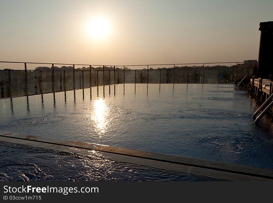 A hazy sun sets over an empty swimming pool on the roof of a city hotel. A hazy sun sets over an empty swimming pool on the roof of a city hotel.