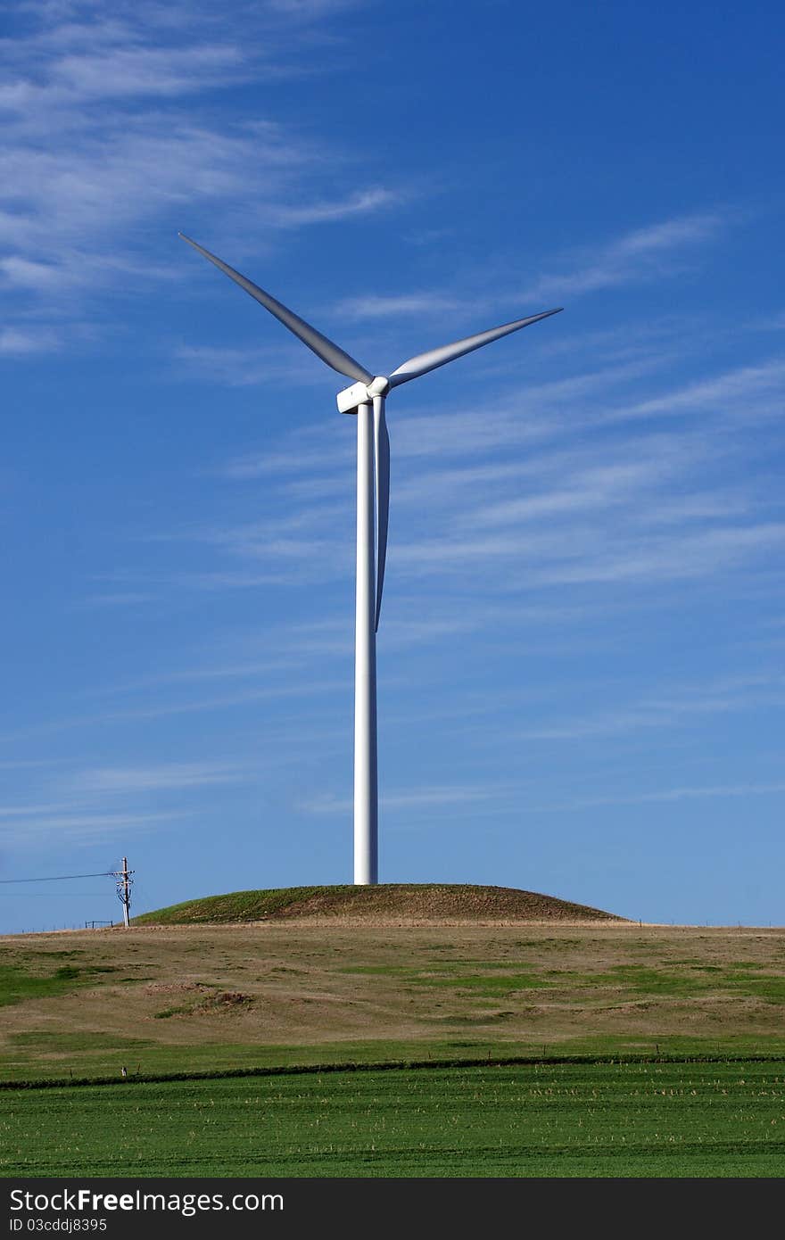 Photograph of a wind turbine against a bright blue sky with wispy clouds. Photograph of a wind turbine against a bright blue sky with wispy clouds.