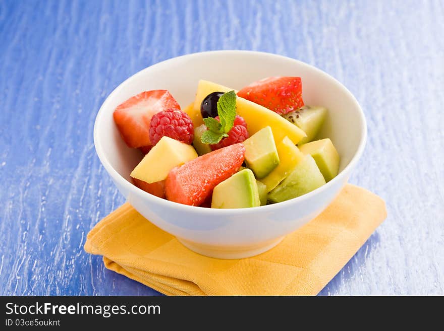 Photo of colorful fruit salad on blue glass table with small mint leaf