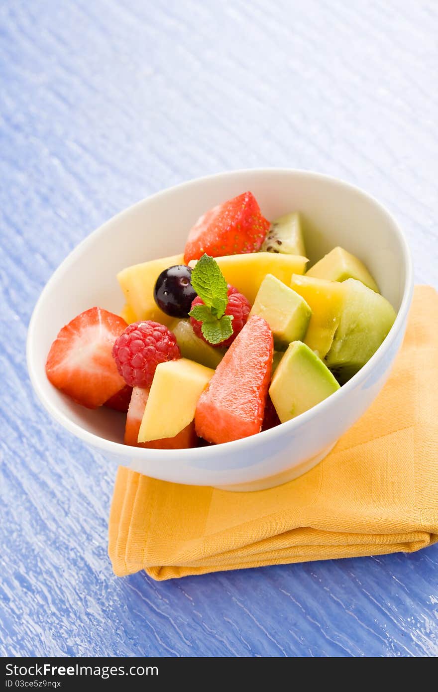 Photo of colorful fruit salad on blue glass table with small mint leaf