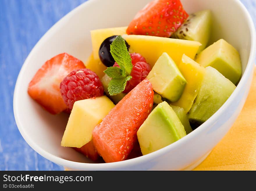 Photo of colorful fruit salad on blue glass table with small mint leaf