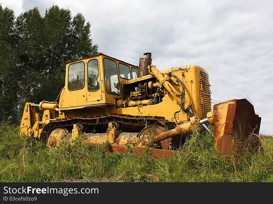 Big old yellow rusty tractor in the field, among the green grass