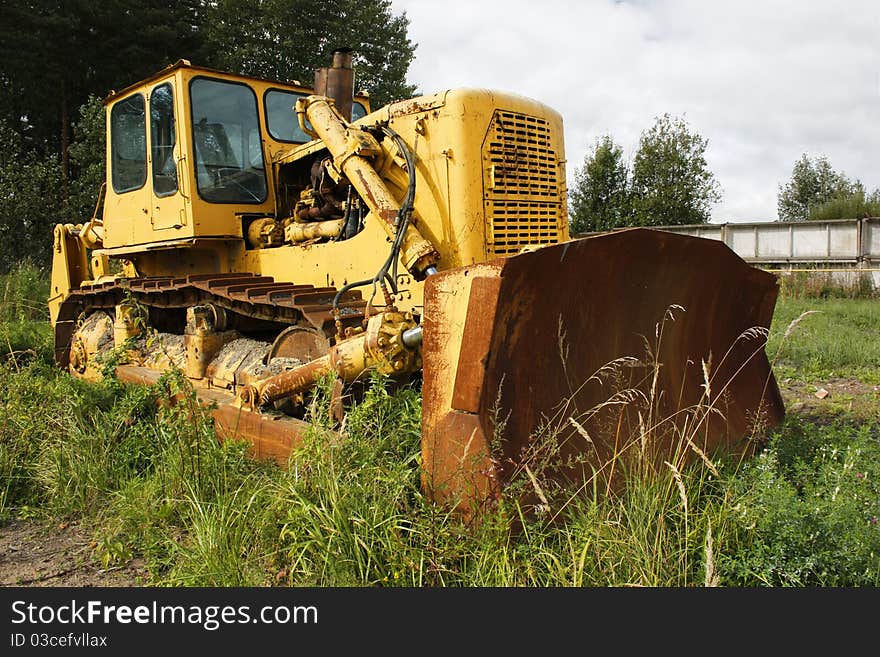 Big old yellow rusty tractor in the field, among the green grass