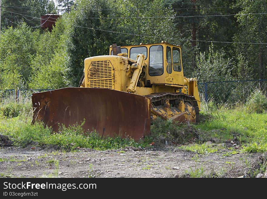 Big old yellow rusty tractor in the field, among the green grass