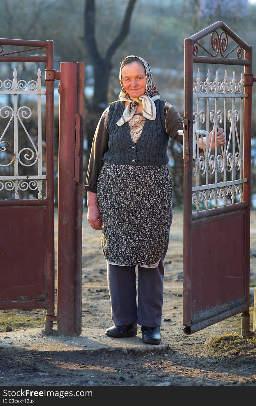 Old village woman standing in front of aged red gate at sunset. Old village woman standing in front of aged red gate at sunset.