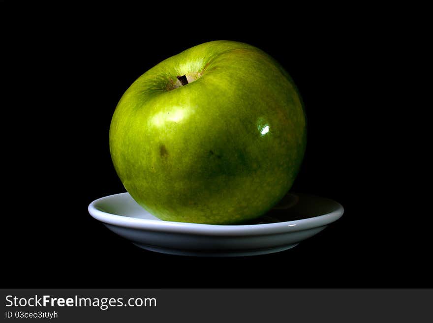 Green apple on a plate on black background