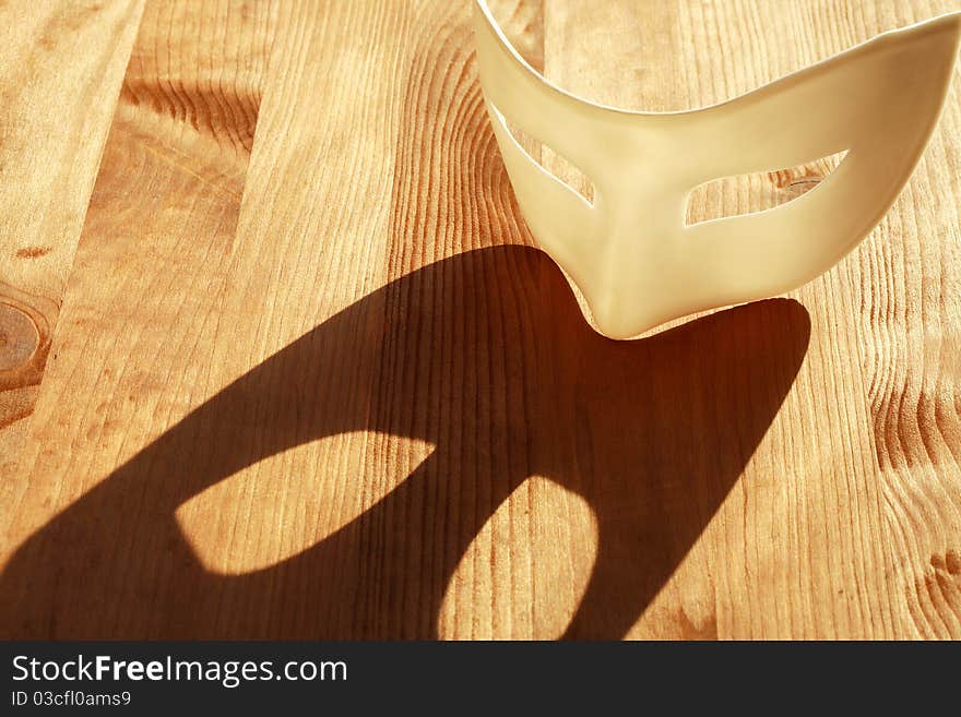 White plastic venetian mask lying on wooden surface with sunbeam and shadow. White plastic venetian mask lying on wooden surface with sunbeam and shadow