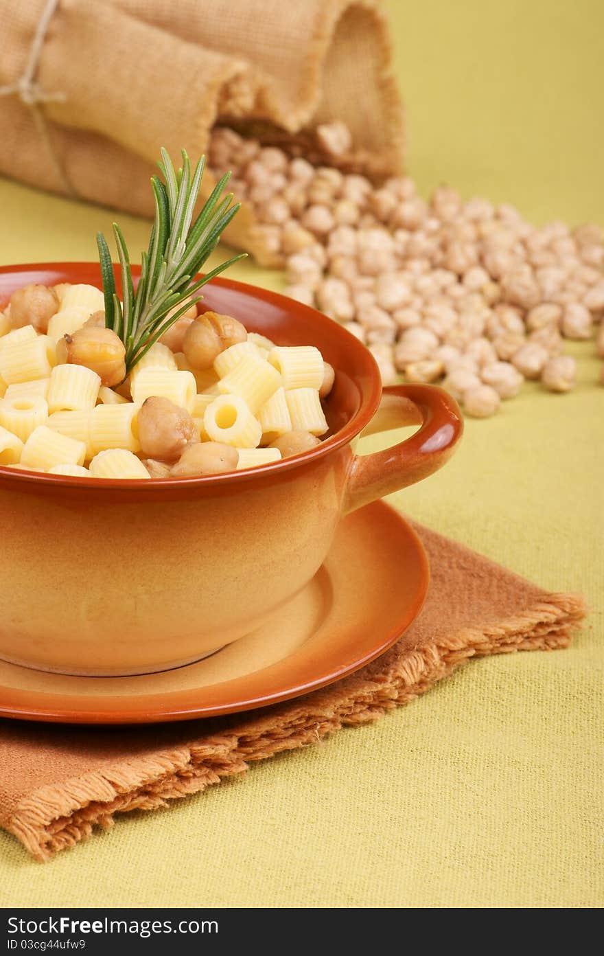 Small thimbles (ditalini) with chickpea and rosemary served in a ceramic bowl. Chickpeas spilling out from a jute bag in the background. Shallow DOF. Small thimbles (ditalini) with chickpea and rosemary served in a ceramic bowl. Chickpeas spilling out from a jute bag in the background. Shallow DOF