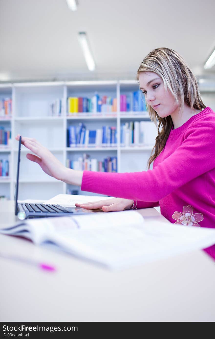 In the library - pretty, female student with laptop and books working in a high school library (color toned image)