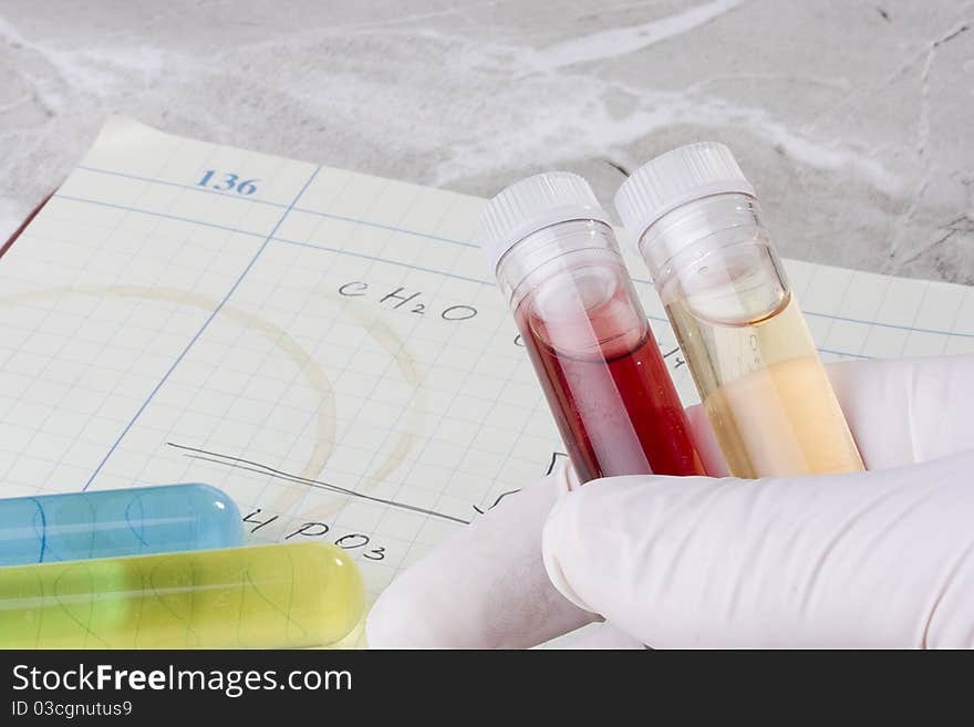 Hand holding test tubes in front of a laboratory notebook. Hand holding test tubes in front of a laboratory notebook.