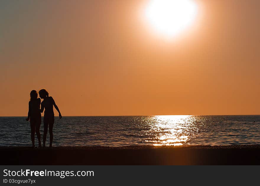 Girls silhouettes standing in front of sea or ocean on sunset