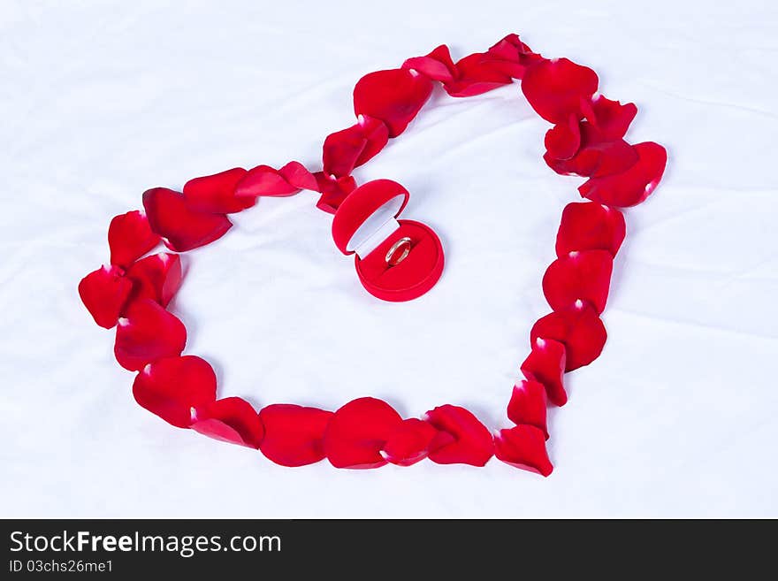 Wedding rings in the red box lie on the bed in the heart of rose petals