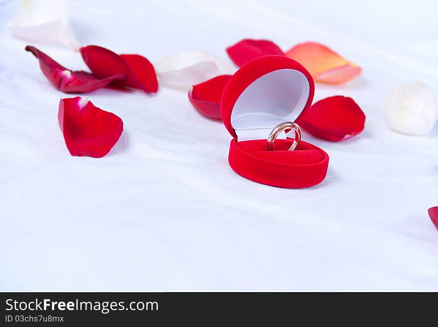 Wedding rings in the red box lie on the bed with rose petals