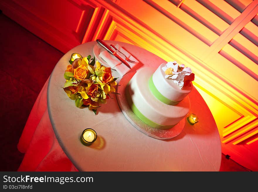 Green and White wedding cake on Red Table surrounded by candles and bride's bouquet