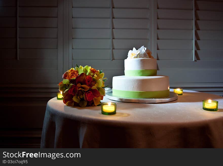 Green and White wedding cake on Table surrounded by candles and bride's bouquet