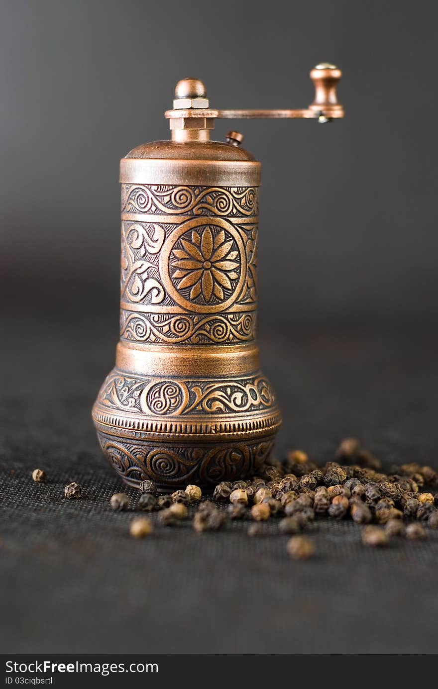 Vintage still life with brass pepper mil standing on the grey background