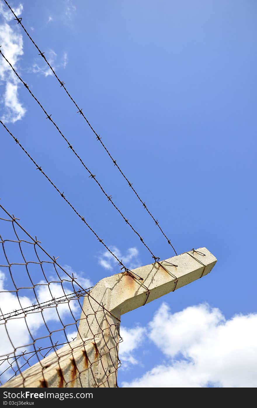 Fence of mesh with barbed wire under blue sky. Fence of mesh with barbed wire under blue sky