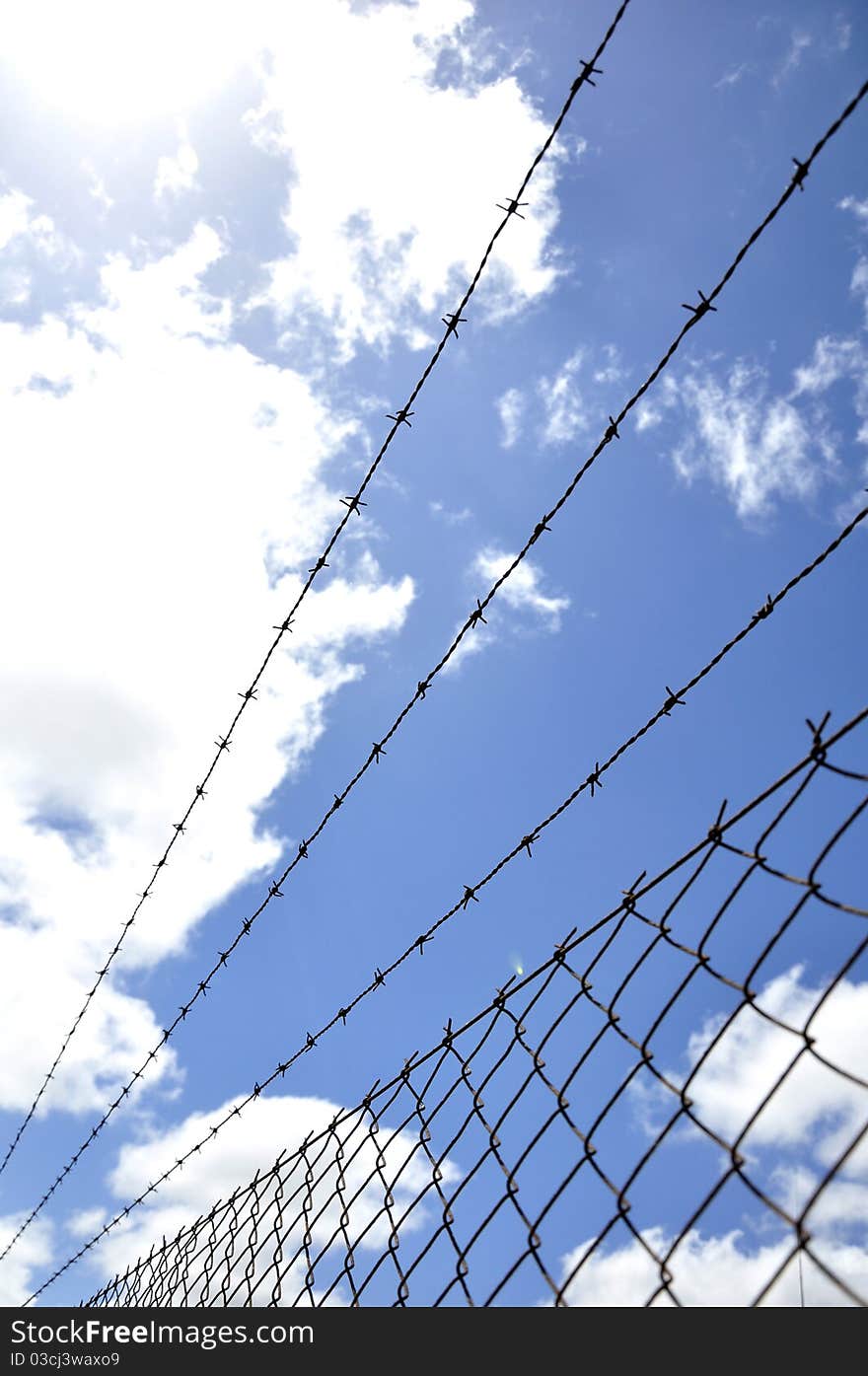 Fence of mesh with barbed wire under blue sky. Fence of mesh with barbed wire under blue sky