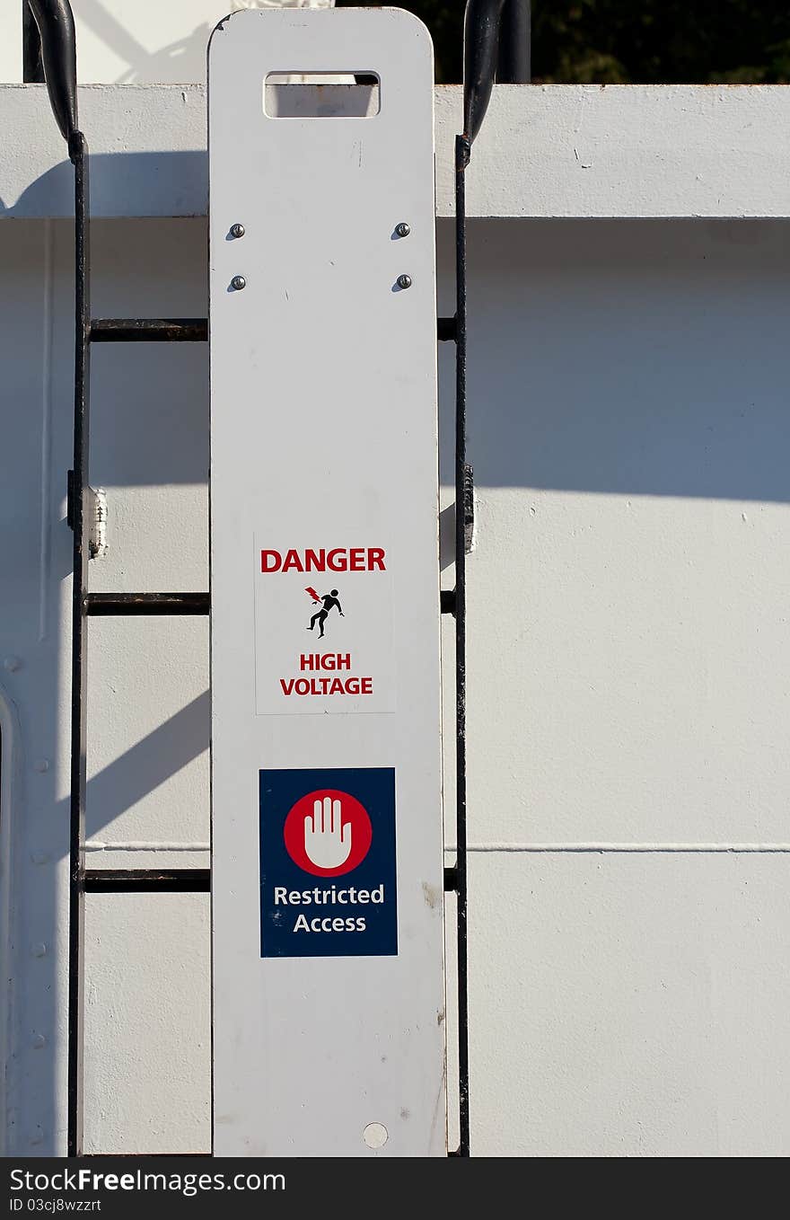 Black rung ladder to upper deck on a passenger ship is barricaded with a metal plate labelled Danger High Voltage Restricted Access.