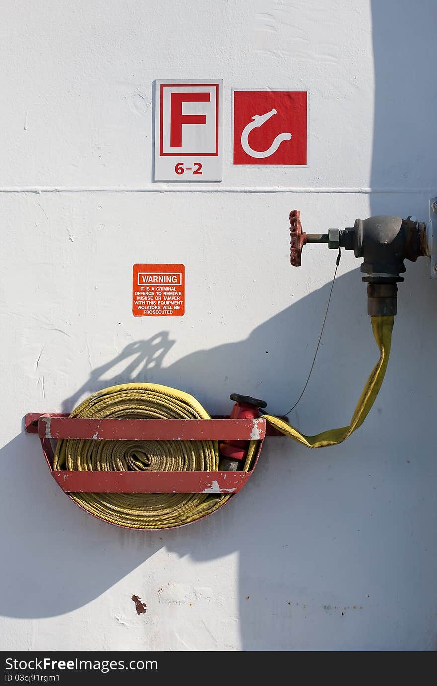 A coiled fire hose in metal cradle is connected to water supply valve at an emergency fire fighting location on a passenger ship. A coiled fire hose in metal cradle is connected to water supply valve at an emergency fire fighting location on a passenger ship.