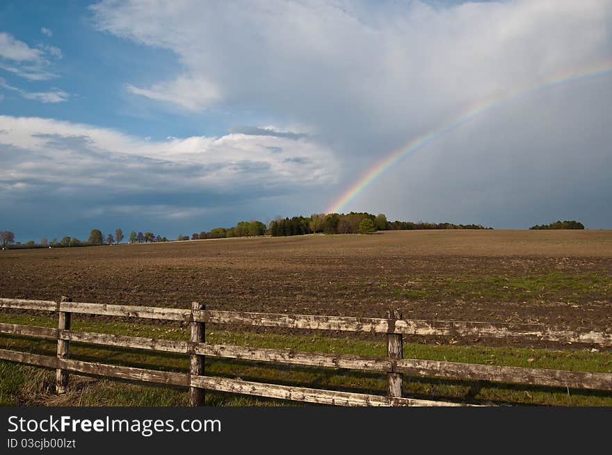 A rainbow and clouds cover the sky above a farm field. A rainbow and clouds cover the sky above a farm field.