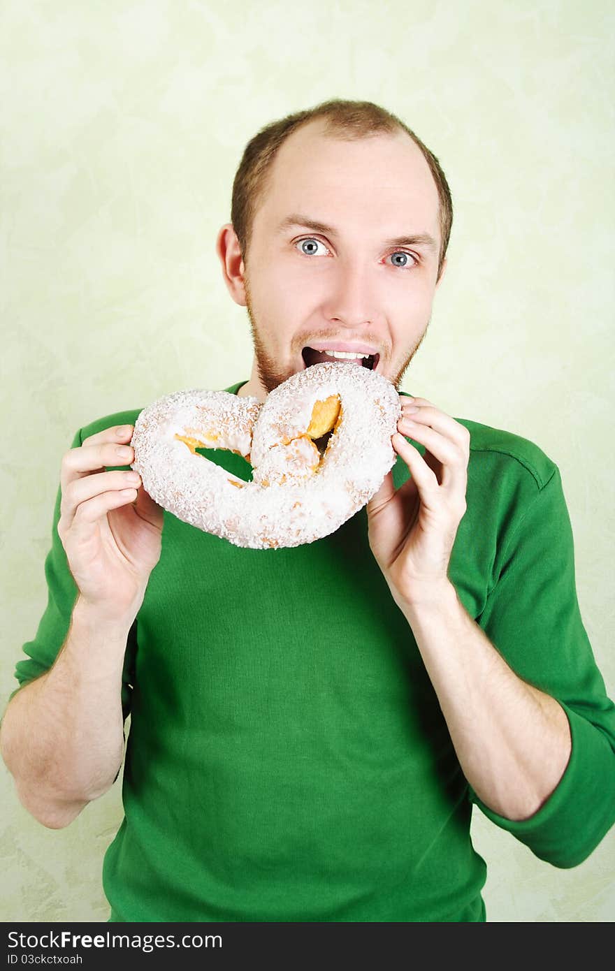 Man in green shirt biting big cracknel with white topping and looking at camera