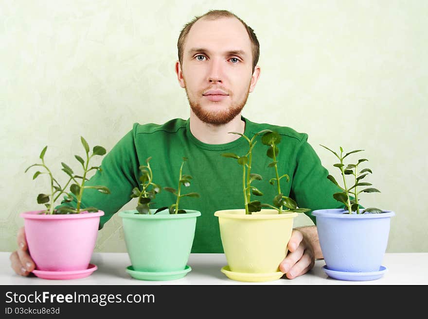 Man in green shirt sitting near table with plants in bright flowerpots. Man in green shirt sitting near table with plants in bright flowerpots